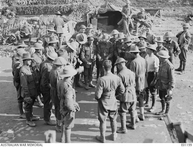 Australian soldiers crouched in a circle playing two-up behind ruined buildings at Ypres, Belgium, in 1917